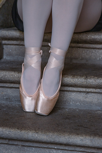 Closeup of ballerina's legs with her pink pointes shoes on. Ballet dancer is sitting on the gray stone steps. Dancer is resting on the stair. Dancer´s feet with pink ballet slippers on.