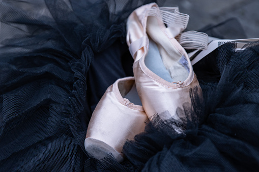 Closeup of the pink ballet pointe shoes laying on the black chiffon Tutu. Two beige ballet slippers on the dark background. Minimalistic concept. Copy Space. Selective focus.