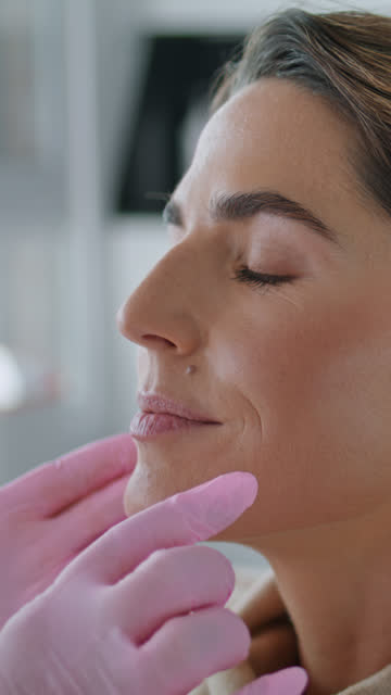 Cosmetologist examining skin woman in clinic vertical closeup. Expert diagnosing