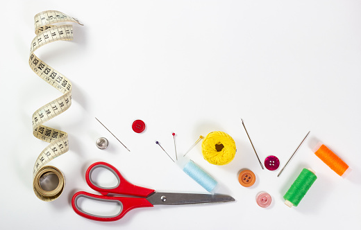 Various sewing accessories (needles, scissors, thread, tape measure, buttons, etc.) on white background.