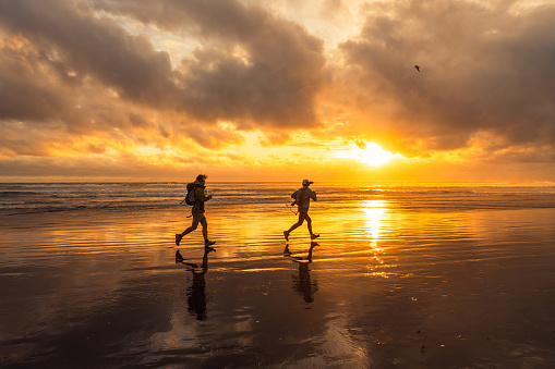 Active senior couple enjoying a day out at beach running along the coast at sunset.