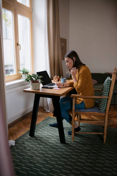istock Young female sitting at desk with laptop writing in a sticky note 2139117660
