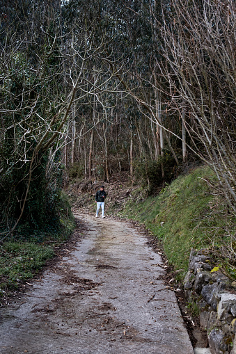 Latino man in camo hoodie, camera, walks forest trail in Asturias.