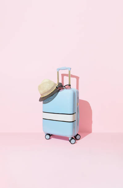 istock Blue suitcase with sunglasses and hat on a pastel pink background with long deep shadows. Travel concept 2139172924