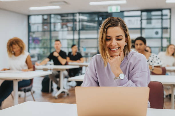 Smiling woman works on laptop during university class