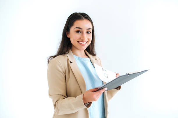 Pleasant pretty brunette indian or arabian business woman, financial consultant, secretary, stands on isolated white background, holding folder with documents and graphs, looks at camera, smile stock photo
