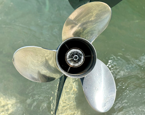 Close up of a very shiny boat propeller reflecting the clear water while the boat is anchored