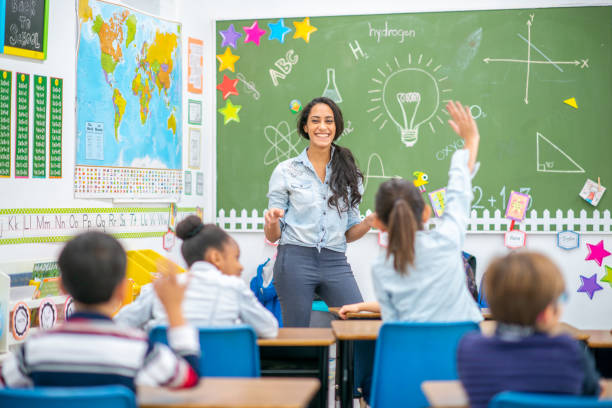 Elementary Science Lession A female teacher of Middle Eastern decent stands at the front of the classroom as she teaches a science lesson to her students. The students are seated at their desks and have hands raised to answer the teachers question. elementary school stock pictures, royalty-free photos & images