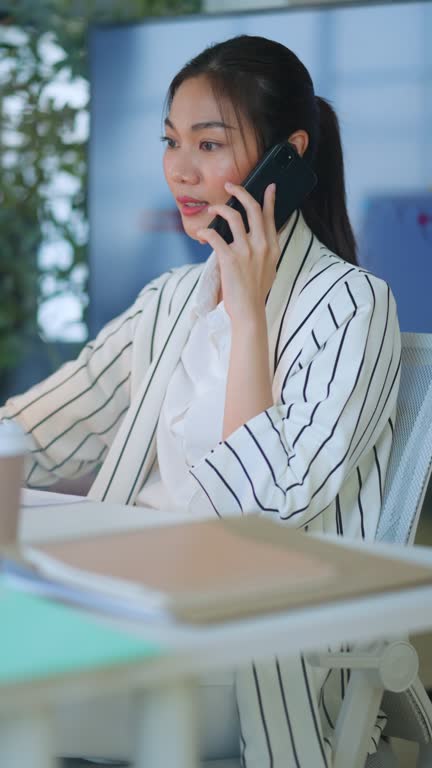 Female professional is with laptop sitting at table.Thoughtful Businesswomaman discussion with a business partner via smartphone while checking finacial annual report on computer screendaylight in a modern office. Business Communication with technology