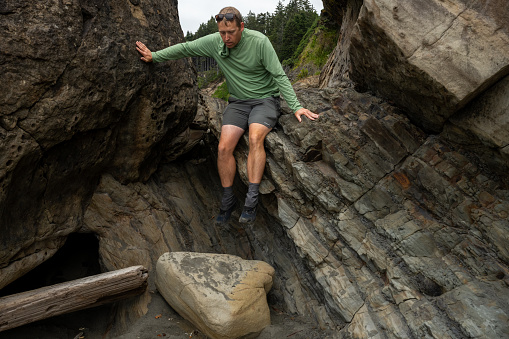 Hiker Climbs Down Rocky Formations Along Beach In Olympic National Park