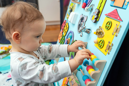 Baby plays with wooden elements on a busy board.