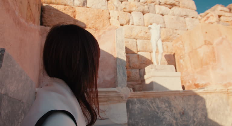Woman watching on ancient marble statue the ruins of ancient greek city