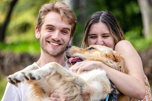 Portrait of happy young couple sitting in the park with their pet Golden Retriever, front view, background with copy space, full frame horizontal composition