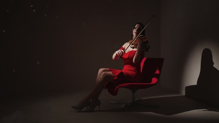 Attractive Young Adult Woman In Red Dress Playing Romantic Melody By Violin In Studio