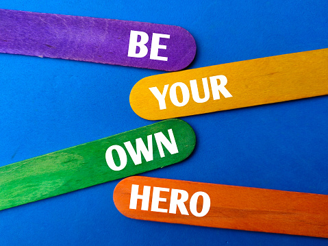 Colored stick with the word BE YOUR OWN HERO on blue background. Business concept.