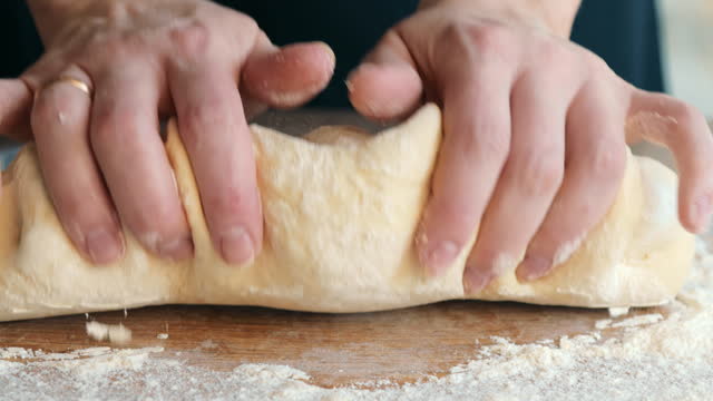 A close-up of a woman pouring flour on a table and kneading the dough with her hands for pizza. The concept of kneading dough.