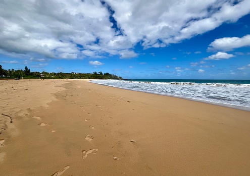 Long range view of a beach on the island of Kauai. Brownish looking sand. Interesting sky overhead.