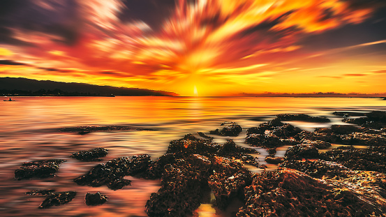 Seascape sunset with dramatic sky, sunbeam , mountain background and rocks by blurred motion and long exposure