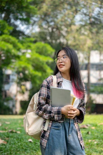 istock A young Asian female college student carrying a backpack and stuff, standing in the campus park. 2139583023