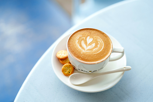 From a high angle view, a cup of coffee latte and crackers are served on a table in a local cafe during the morning.