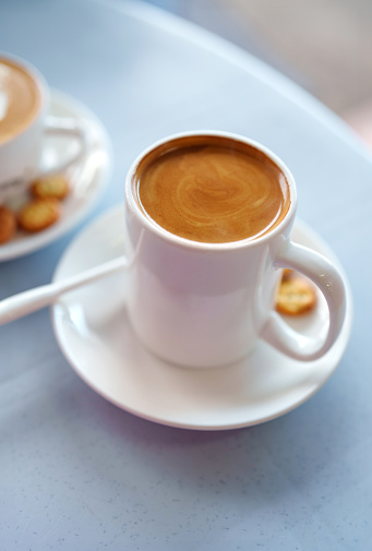 A high-angle view shows a cup of milk coffee served with some crackers on a table.