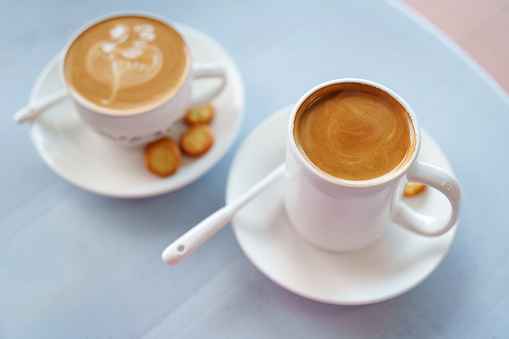 A high-angle view shows two cup of milk coffee served with some crackers on a table.