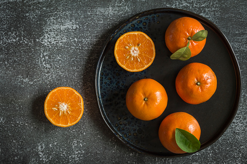 Fresh mandarin oranges cut in half in a black plate on a gray background.