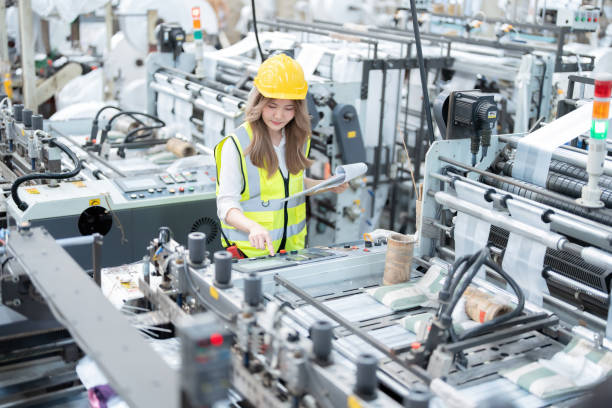 istock Asian female engineer holds a list of notes and presses buttons on a computerized machine producing robots and cars with circuit boards in a global manufacturing and export industry. 2139755091