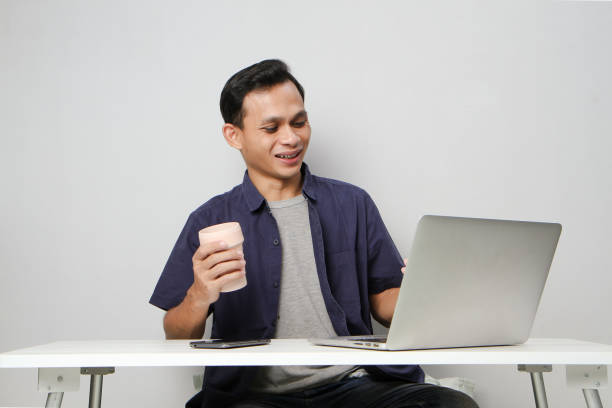 istock joyfull happy asian man at workplace while sitting in front of laptop computer. on isolated background 2139756167