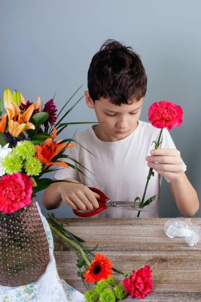 young florist is arranging flowers into a bouquet in a vase at home. - carnation mothers day florist flower ストックフォトと画像