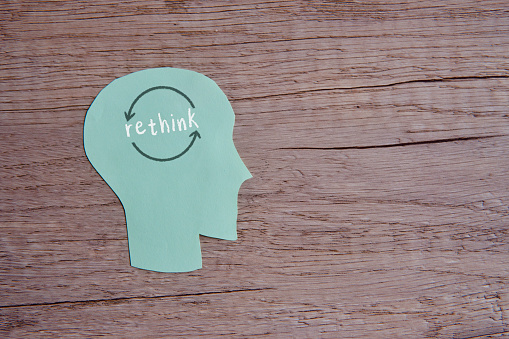 A conceptual image with the word rethink written across a paper cutout head on wooden table with copy space.