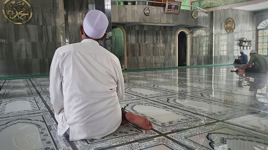 A muslim man in sits in quiet contemplation, practicing his faith in the peaceful expanse of the mosque's interior