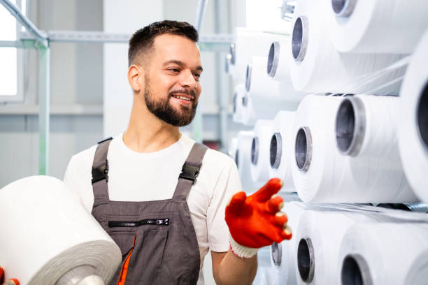 istock Textile factory worker changing thread spool on industrial knitting machine. 2139910255