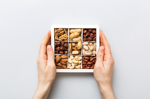 Young woman holding box with different nuts, closeup. Close up, copy space, top view, flat lay. Walnut, pistachios, almonds, hazelnuts and cashews.