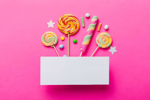 Flat lay holiday composition. Paper blank, lollipop, birthday decorations on Colored background. Top view, copy space for text.
