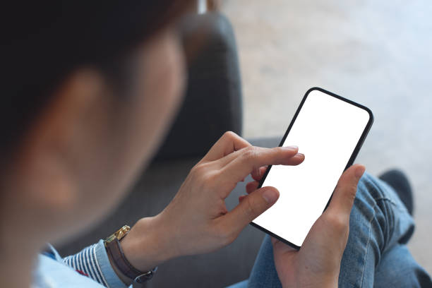 istock Mockup, woman's hands holding mobile phone with finger touching on blank screen. Woman using smartphone, looking at the screen, over shoulder view 2139943209