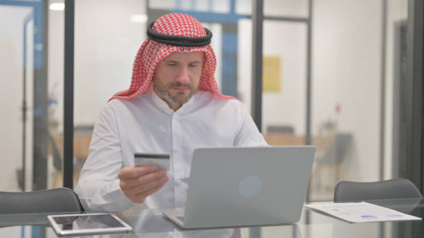 istock Arab Man Shopping Online on Laptop in Office 2139947053