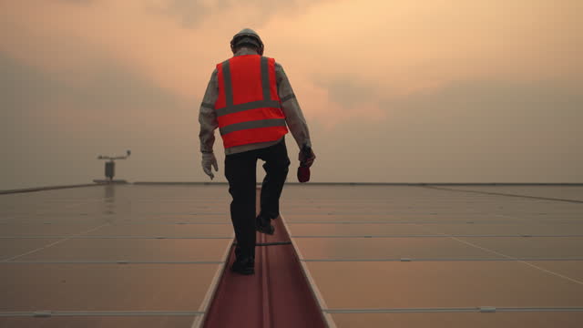 A man in a safety vest is walking on a metal walkway