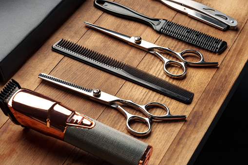 A set of professional barber tools, including scissors, clippers, and combs, neatly arranged on a polished wooden surface, highlighting the essentials for a precise mens grooming session.