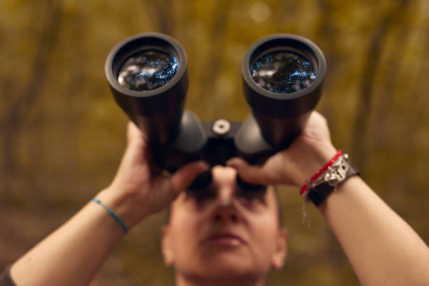 Woman using binoculars for birdwatching and observing other animals in nature.