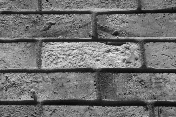 A stark black and white image capturing the textures and patterns of a weathered brick wall. The bricks are irregularly shaped and worn, with visible mortar filling the gaps. Light and shadow play across the rough surface, highlighting the rugged beauty of the wall.
