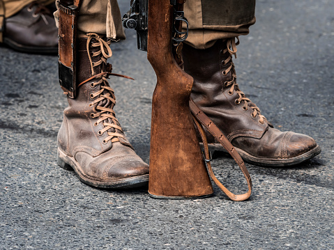 Sainte Mere L'Eglise, Normandy, France - June 6, 2023. Second world war commemoration. Military camp reconstitution. Unidentified vintage shoes close up and rifle during second world war