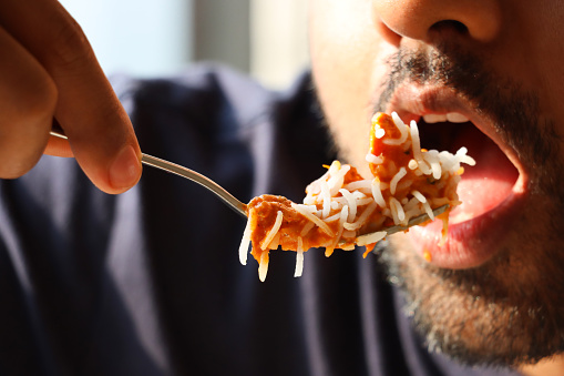 Stock photo showing close-up view of an Indian man about to eat a forkful of homemade Indian butter chicken with rice.