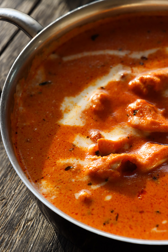 Stock photo showing close-up, elevated view of metal bowl of Indian butter chicken curry sauce with cream drizzled on the surface.