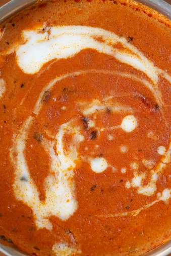 Stock photo showing close-up, elevated view of metal bowl of Indian butter chicken curry sauce with cream drizzled on the surface.