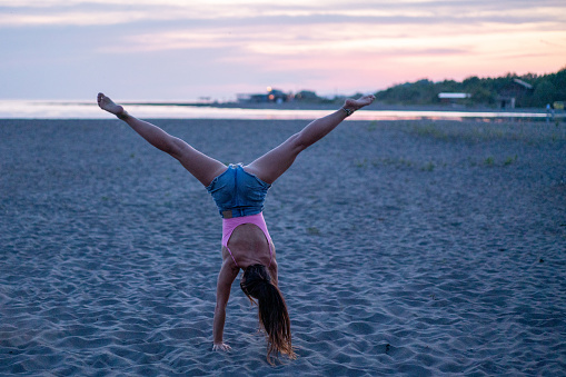 Full length of a woman does a handstand on the beach during a summer day