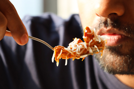 Stock photo showing close-up view of an Indian man about to eat a forkful of homemade Indian butter chicken with rice.