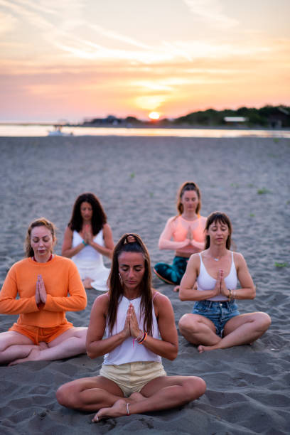 group of females meditating on the beach - zen like nature breathing exercise sitting stock-fotos und bilder