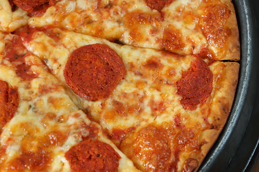 Stock photo showing close-up, elevated view of a metal pizza pan displaying a pepperoni pizza, topped with a rich tomato sauce and melted buffalo mozzarella with a crispy crust.
