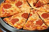 Full frame image of sliced pepperoni pizza in metal pizza pan, circular slices of pepperoni sausage, melted golden buffalo mozzarella cheese and rich tomato marinara sauce topping, elevated view, focus on foreground